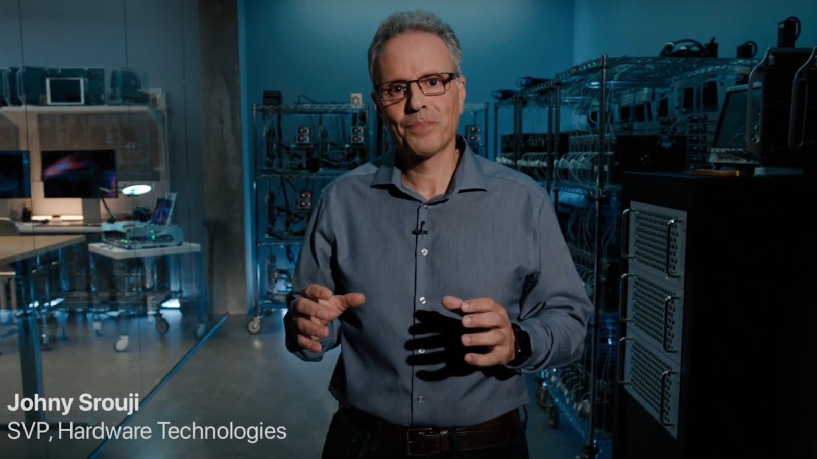 من موقع فون إسلام: رجل يقف في مختبر تكنولوجي مع معدات كمبيوتر، يرتدي نظارات وقميص أزرق. نص على الشاشة يقول: "جوني سروجي، نائب الرئيس الأول، تقنيات الأجهزة.