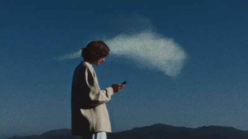 من موقع فون إسلام: ينظر الشخص الواقف في الهواء الطلق إلى هاتفه ويتفحص تطبيق YouWare، بينما تظهر سحابة صغيرة في السماء فوق رأسه وخلفه، كما لو أن فكرة - مستوحاة من التكنولوجيا قد تشكلت للتو.