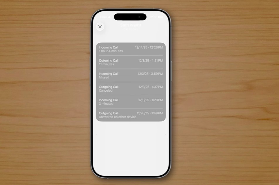 من موقع فون إسلام: هاتف ذكي، من المحتمل أن يكون هاتفًا ذكيًا، من المحتمل أن يكون الآي فون الآي فون، يستند على سطح خشبي، يعرض سجل مكالمات بتفاصيل المكالمات الواردة والصادرة - مع إبراز مدد المكالمات الواردة والصادرة والطوابع الزمنية، وربما يعرض ميزات خفية تم تقديمها في نظام iOS 26.