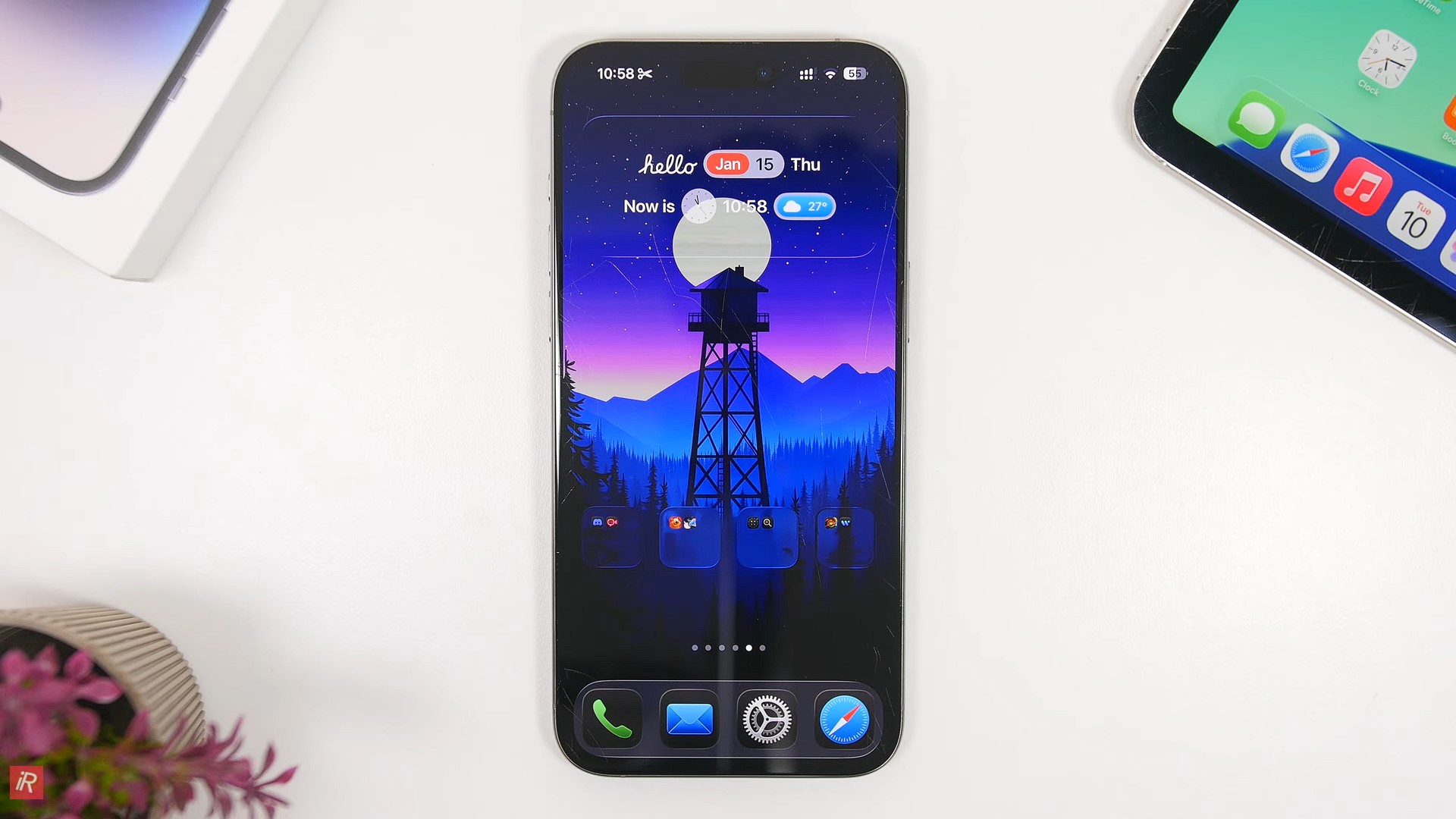 من موقع فون إسلام: يعرض هاتف ذكي، ربما يعمل بنظام آي فون 17 أو يستكشف حيل iOS، شاشة رئيسية مع خلفية برج المراقبة، وثلاث فتحات فارغة للقطعة وأربعة أيقونات تطبيقات في قفص الاتهام. توجد أجهزة أخرى ونبتة على سطح أبيض.