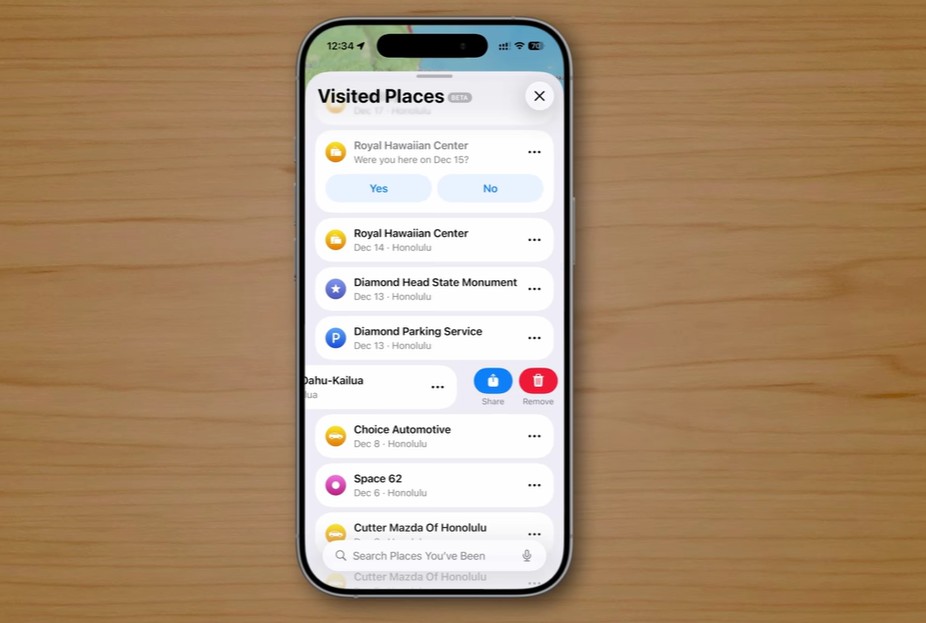 من موقع فون إسلام: يعرض الهاتف الذكي الذي يعمل بنظام التشغيل iOS 26 شاشة "الأماكن التي تمت زيارتها" مع قائمة بالمواقع وخيارات التاريخ لتأكيد الزيارات. يرتكز الآي-فون على سطح خشبي.