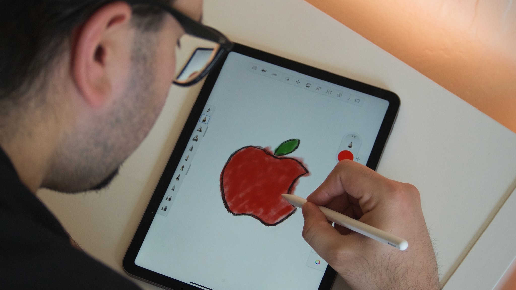 Z serwisu PhoneIslam: Ktoś używa rysika Apple Pencil, aby narysować na ekranie tabletu czerwone jabłko z zielonym liściem.