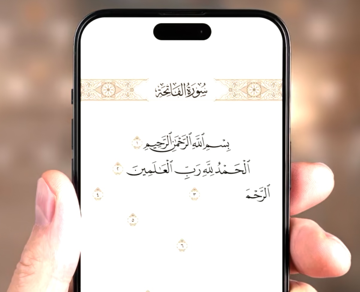 من موقع فون إسلام: يد تحمل هاتفًا ذكيًا يعرض على الشاشة النص العربي لسورة الفاتحة من القرآن الكريم مع تسليط الضوء على سهولة الوصول إليها من خلال متاجر التطبيقات.