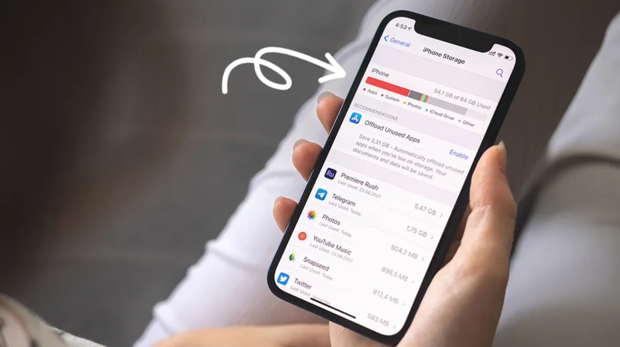 من موقع فون إسلام: شخص يحمل جهاز iPhone يعرض شاشة تخزين iPhone، والتي تعرض تفاصيل استخدام التخزين وقائمة بالتطبيقات مع استهلاكها للتخزين - وهي طريقة مفيدة لتشخيص أسباب مشكلة التخزين.