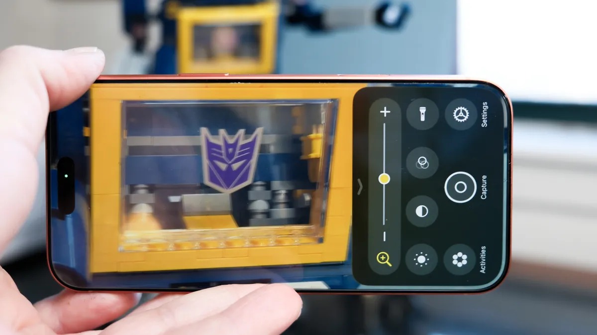 من موقع فون إسلام: يد تحمل واجهة تطبيق كاميرا تحمل صورة يد تحمل واجهة تطبيق كاميرا تظهر فيها واجهة تطبيق كاميرا باللونين الأصفر والأزرق مع شعار ديسيبتيكونز باللون الأرجواني، وتبرز مزايا التحكم بالكاميرا.