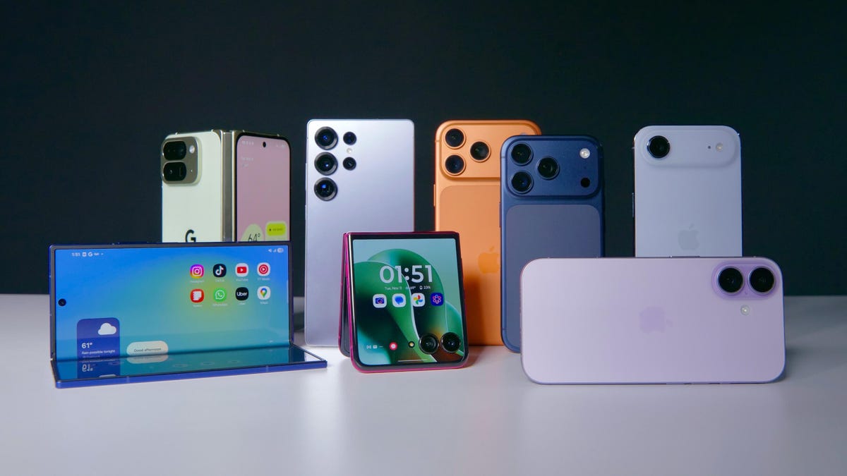 من موقع فون إسلام: يتم عرض العديد من هواتف ذكية عصرية بألوان وتصاميم مختلفة، بما في ذلك الموديلات القابلة للطي والموديلات القياسية، على سطح أبيض على خلفية داكنة. تتميز المجموعة بعلامات تجارية شهيرة مثل آيفون-فون.