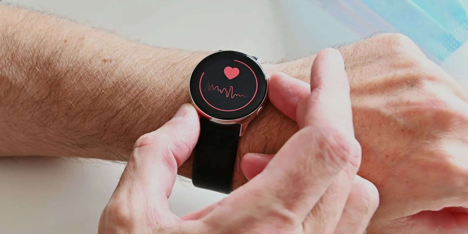 من موقع فون إسلام: يقوم الشخص بفحص معدل ضربات قلبه على ساعة ذكية تعرض رمز القلب والرسم البياني للنبض على معصمه، ومزامنة البيانات بسلاسة مع نظام التشغيل iOS 26.3 لتتبع الحالة الصحية في الوقت الفعلي.