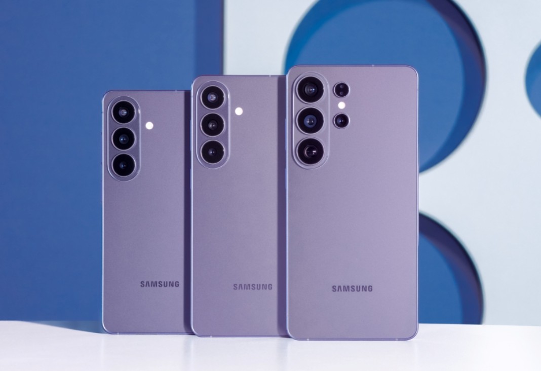 من موقع فون إسلام: ثلاثة هواتف ذكية بنفسجية اللون من سامسونج تقف في وضع مستقيم جنباً إلى جنب، وتظهر جوانبها الخلفية بعدسات كاميرات متعددة، على خلفية هندسية زرقاء وبيضاء مستوحاة من مؤتمر سامسونج.