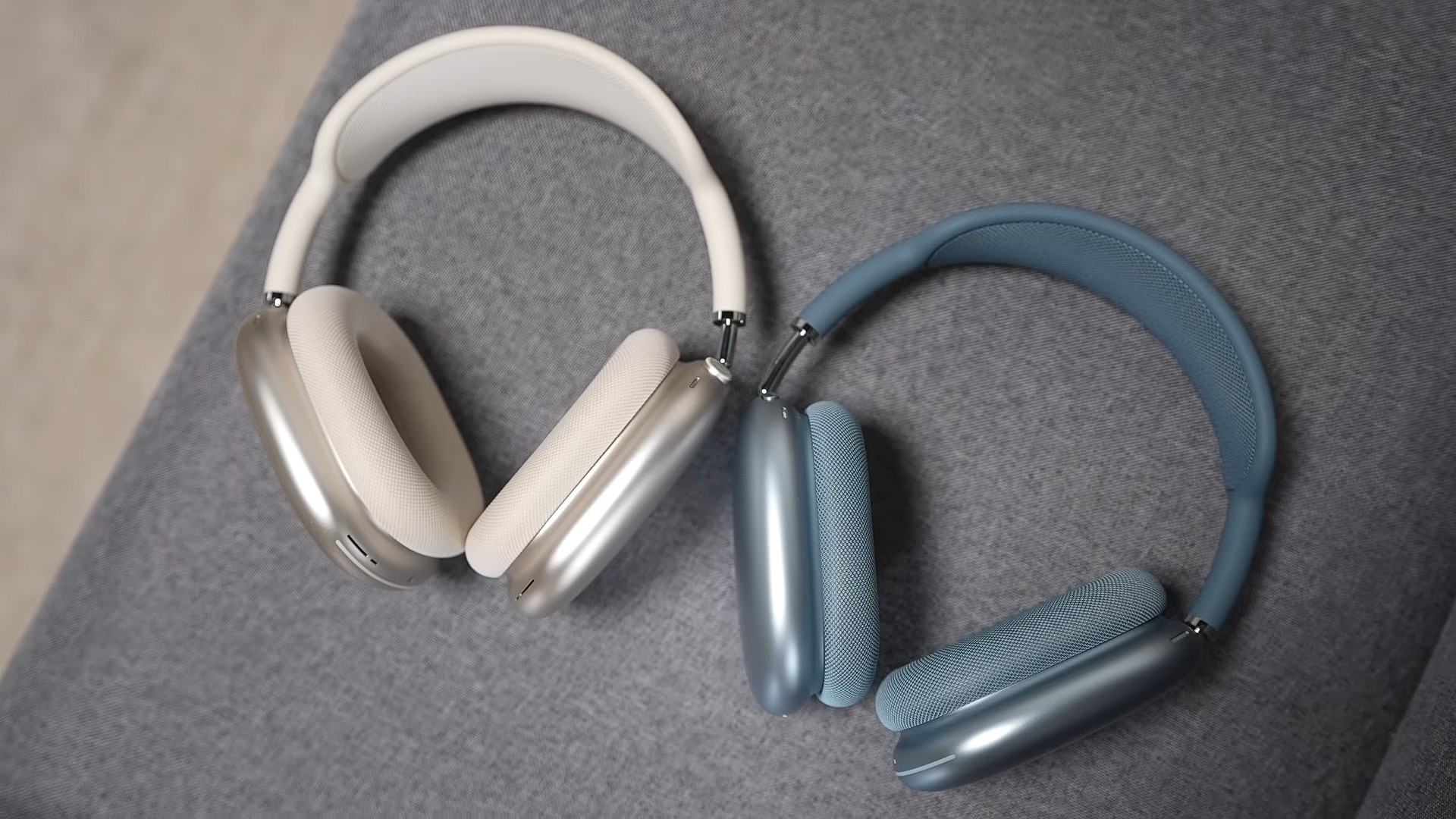 من موقع فون إسلام: زوجان من سماعات الرأس التي توضع فوق الأذن، بما في ذلك سماعة AirPods Max 2 باللونين الفضي والأبيض وأخرى باللون الأزرق، ترتكز على سطح قماشي رمادي.