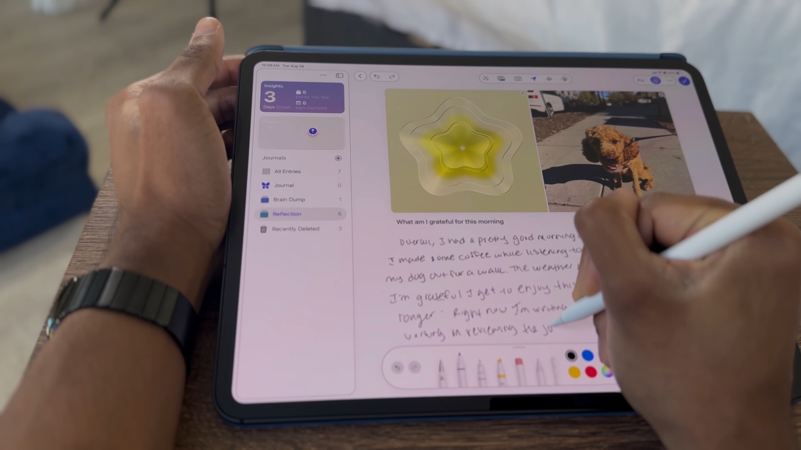 من موقع فون إسلام: شخص يستخدم قلمًا لكتابة ملاحظات مكتوبة بخط اليد على جهاز لوحي يعرض إدخالات اليوميات في تطبيق اليوميات مع صورة كلب وصورة بيضة مكسورة في قالب على شكل زهرة.