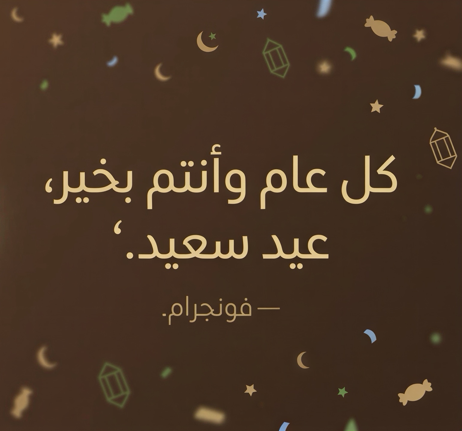 من موقع فون إسلام: نص باللغة العربية على خلفية بنية اللون مع رسوم توضيحية لقصاصات الورق والفانوس والحلوى، نصه "كل عام وأنتم بختمير عيد سعيد وهديّة العيد لكم من آيفون إسلاميـون ـ فونجرام.