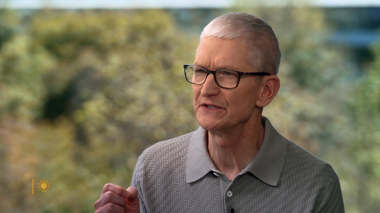 من موقع فون إسلام: شخص ذو شعر رمادي قصير ونظارات يرتدي قميصاً رمادي اللون بياقة رمادية ويتحدث بينما يشير بيده اليمنى. تظهر أشجار غير واضحة في الخلفية.