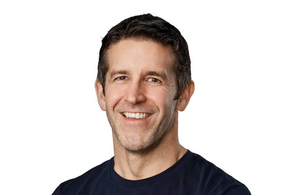 من موقع فون إسلام: رجل في منتصف العمر بشعر داكن قصير ولحية مشذبة يبتسم للكاميرا على خلفية فاتحة عادية، يشبه جون توسيرن خليفة تيم كوك في سلوكه المهني.