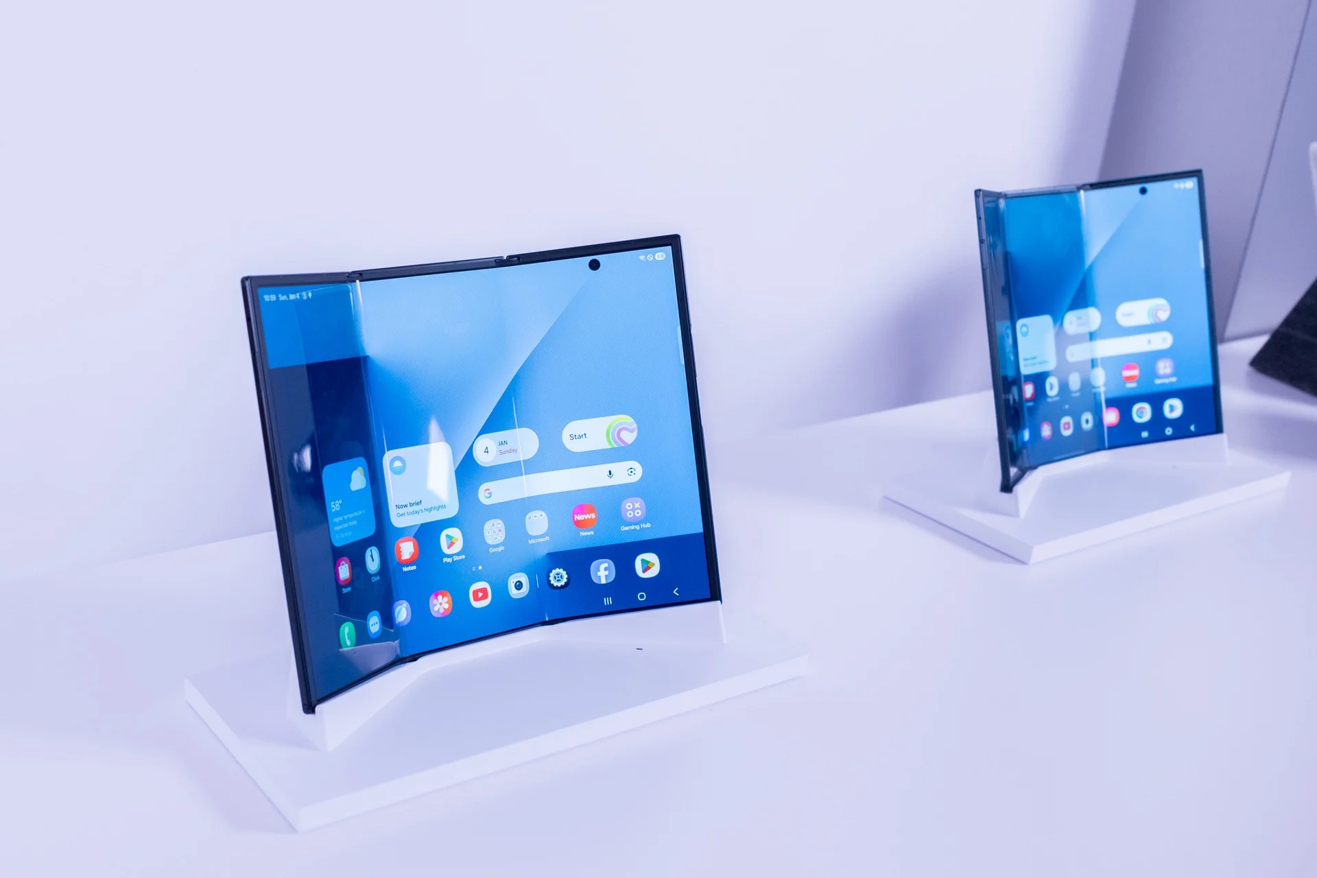 من موقع فون إسلام: تم عرض جهازين لوحيين قابلين للطي، بما في ذلك جهاز سامسونج جالاكسي Z TriFold، على حوامل بيضاء، حيث يظهر تصميمهما المنحني والمطوي جزئياً وشاشتيهما الرئيسيتين.