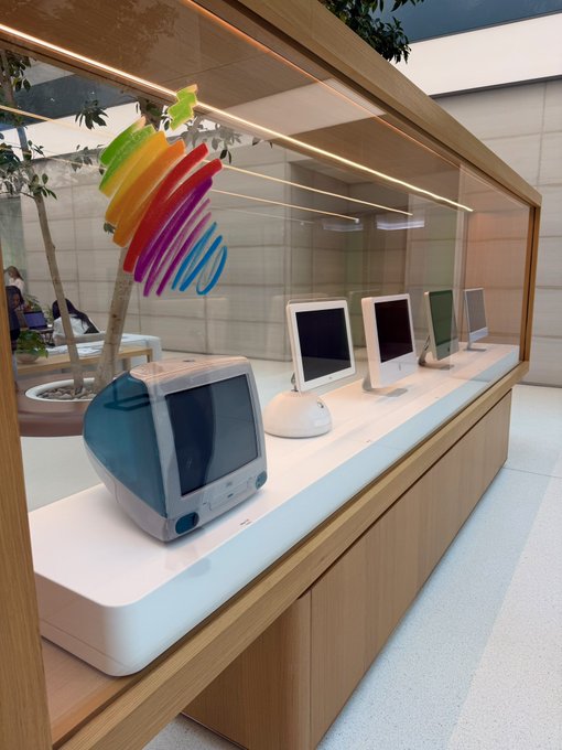 من موقع فون إسلام: علبة عرض تحتوي على العديد من أجهزة كمبيوتر Apple القديمة مرتبة في صف واحد، وتتميز بشعار Apple الملون على الزجاج، وتحتفل احتفالاً بالذكرى الخمسين.