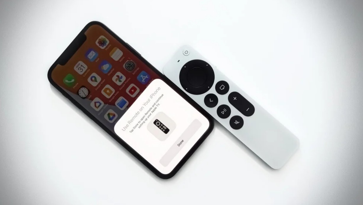 من موقع فون إسلام: شاشة عرض شاشة إعداد للإقران بجهاز تحكم عن بُعد، موضوعة بجانب جهاز تحكم عن بُعد لتلفزيون Apple على سطح أبيض.