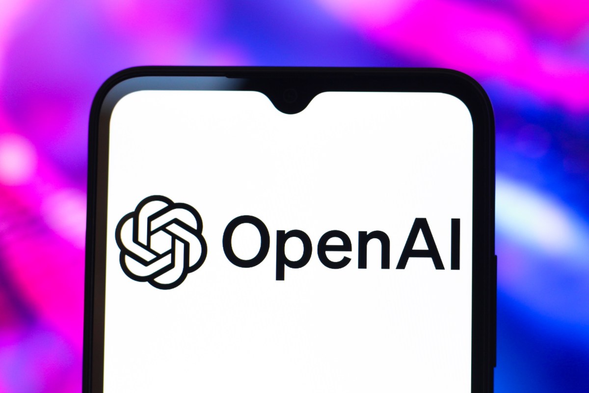 من موقع فون إسلام: تعرض شاشة الهاتف الذكي شعار ونص OpenAI، مع خلفية ضبابية باللونين الوردي والأزرق.