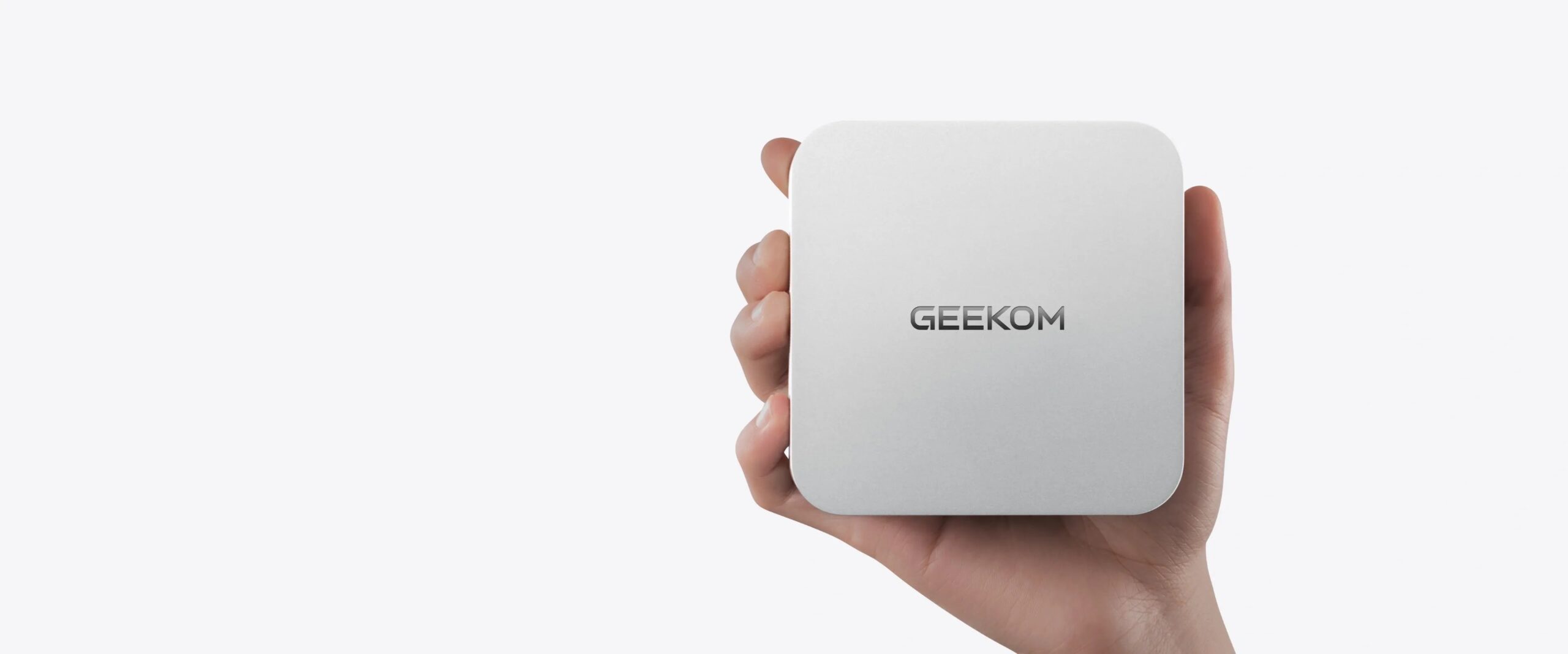من موقع فون إسلام: يد تحمل جهاز GEEKOM A6 صغير الحجم ومربـع الشكل، جهاز GEEKOM A6 مع اسم علامته التجارية الظاهر على خلفية بيضاء سادة - كمبيوتر ويندوز أو كمبيوتر بجانب الماكـر.