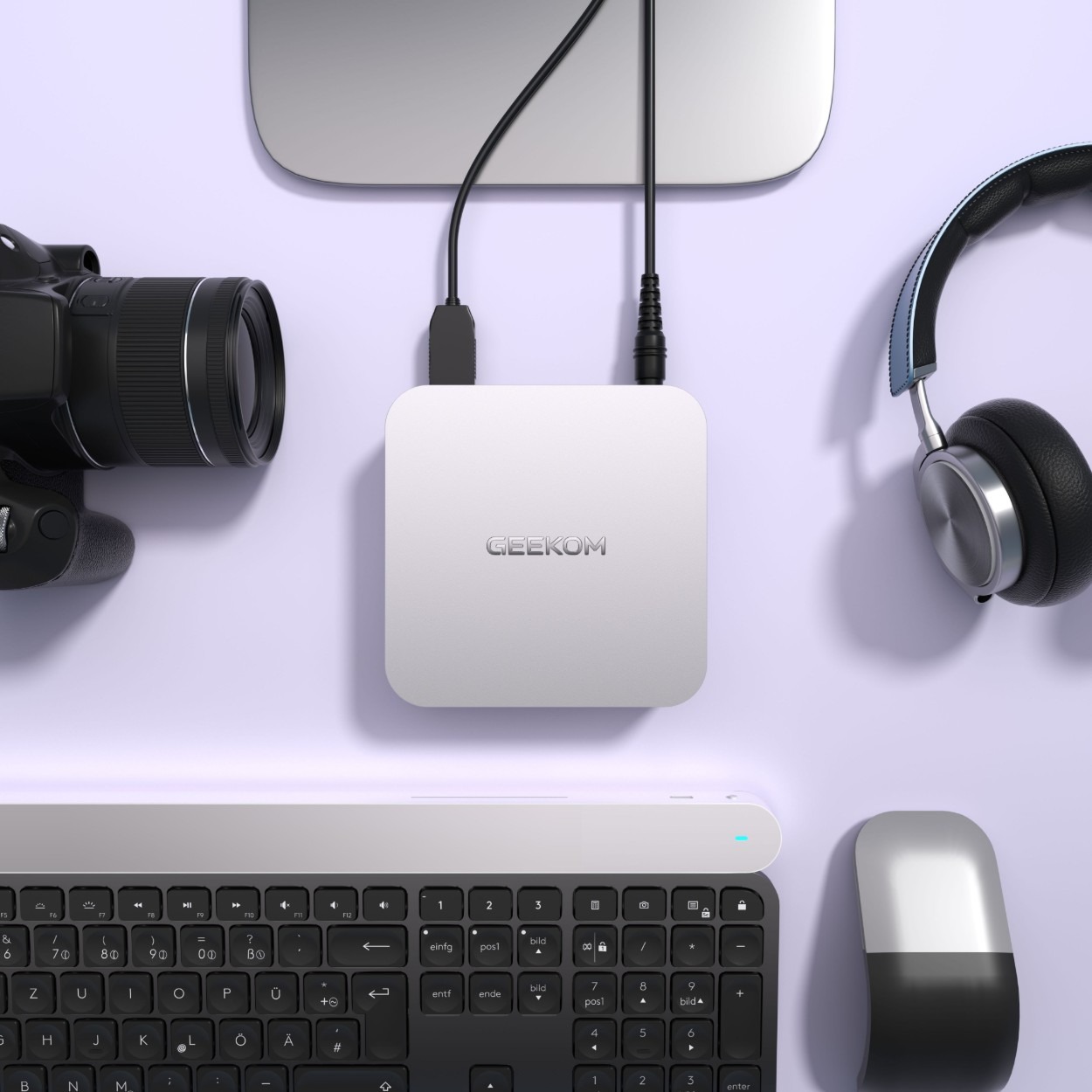 من موقع فون إسلام: جهاز كمبيوتر فضي صغير الحجم من نوع جايكوم A6 على مكتب محاط بلوحة مفاتيح وماوس وكاميرا وسماعات رأس وجهاز إلكتروني آخر-مثالي لمن يبحث عن أفضل كمبيوتر ويندوز للمكتب أو العمل اليومي.