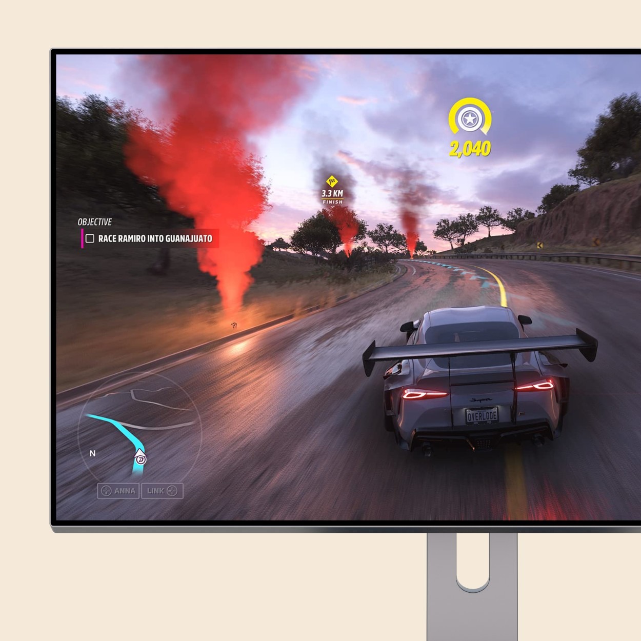 من موقع فون إسلام: لعبة فيديو للسباق تظهر سيارة رياضية تسير على طريق مبلل عند غروب الشمس، مع وجود شعلات مضيئة حمراء على طول الطريق وأهداف اللعبة معروضة على الشاشة، وتعمل بسلاسة على جهاز GEEKOM A6 كمبيوتر كمبيوتر ويندوز بجانب الماكيت.