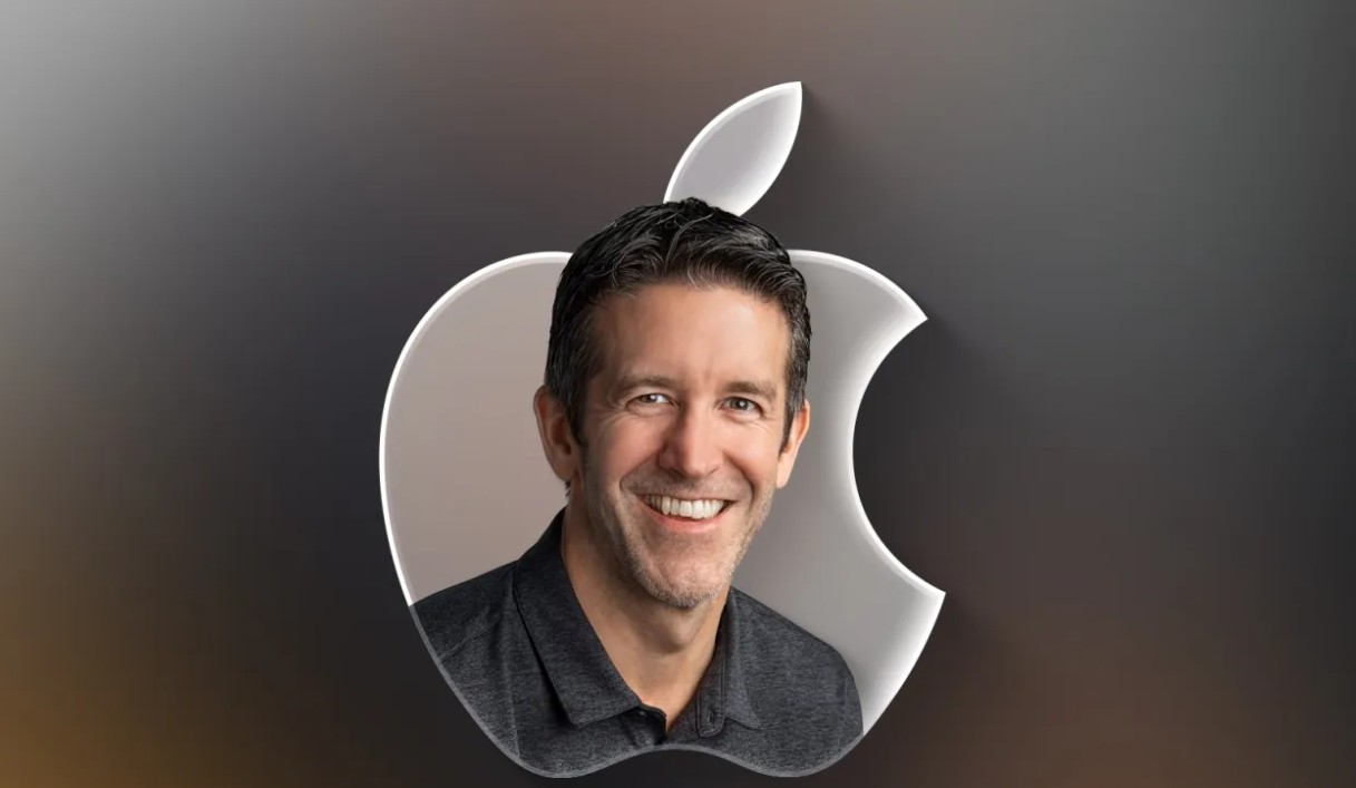 من موقع فون إسلام: رجل مبتسم، يرتدي قميصًا داكن اللون، يظهر في الصورة أمام شعار أبل فضي كبير على خلفية متدرجة اللون - من المحتمل أن يكون جون تيرنوس المعروف بقيادته في شركة أبل.