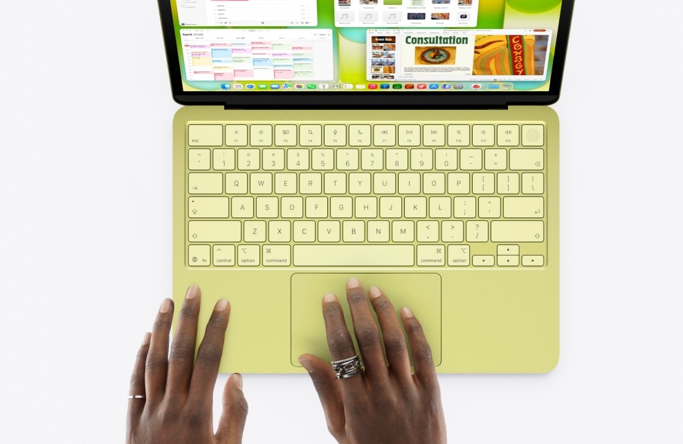 من موقع فون إسلام: شخص يكتب على لوحة مفاتيح ماك بوك نيو باللون الأصفر والأخضر، مع وجود عدة نوافذ مفتوحة على الشاشة، ويتم عرضها من الأعلى.