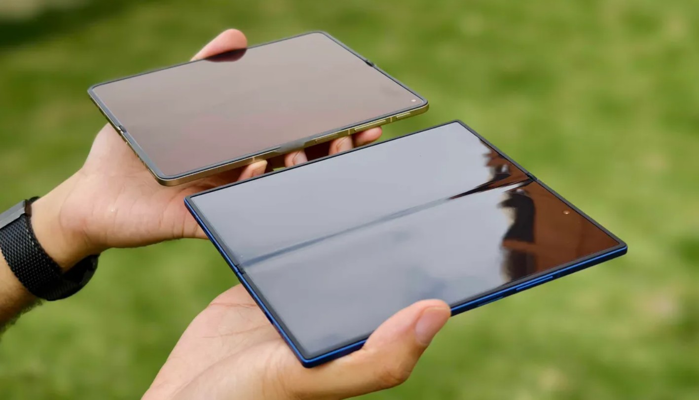 من موقع فون إسلام: يدان ممسكتان بشاشتين مفتوحتين بشاشة كبيرة معروضة في الهواء الطلق على خلفية خضراء غير واضحة.