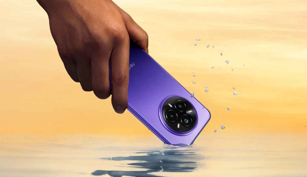 من موقع فون إسلام: يد تحمل يدًا تحمل آليًا أرجوانيًا مزودًا بثلاث كاميرات خلفية، تغمسها جزئيًا في الماء على خلفية صفراء برتقالية.