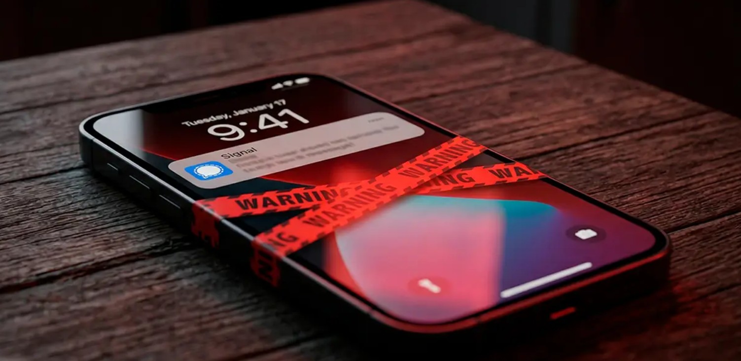 من موقع فون إسلام: يتم تغليف الهاتف الذكي الذي يعرض إشعار تطبيق Signal بشريط تحذير أحمر، مما يشير إلى أن الرسائل ثغرة غير متوفرة، ويتم وضعه على سطح خشبي.