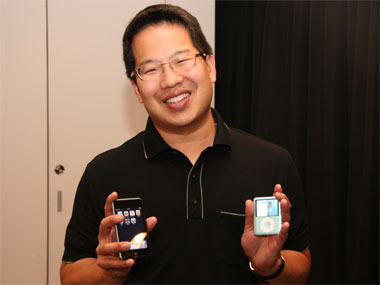 من موقع فون إسلام: رجل يرتدي نظارات وقميصًا أسود ويحمل هاتفًا ذكيًا في يده اليمنى ومشغل MP3 في يده اليسرى، ويبتسم للكاميرا وهو يتابع أخبار هامش لشهر أبريل.