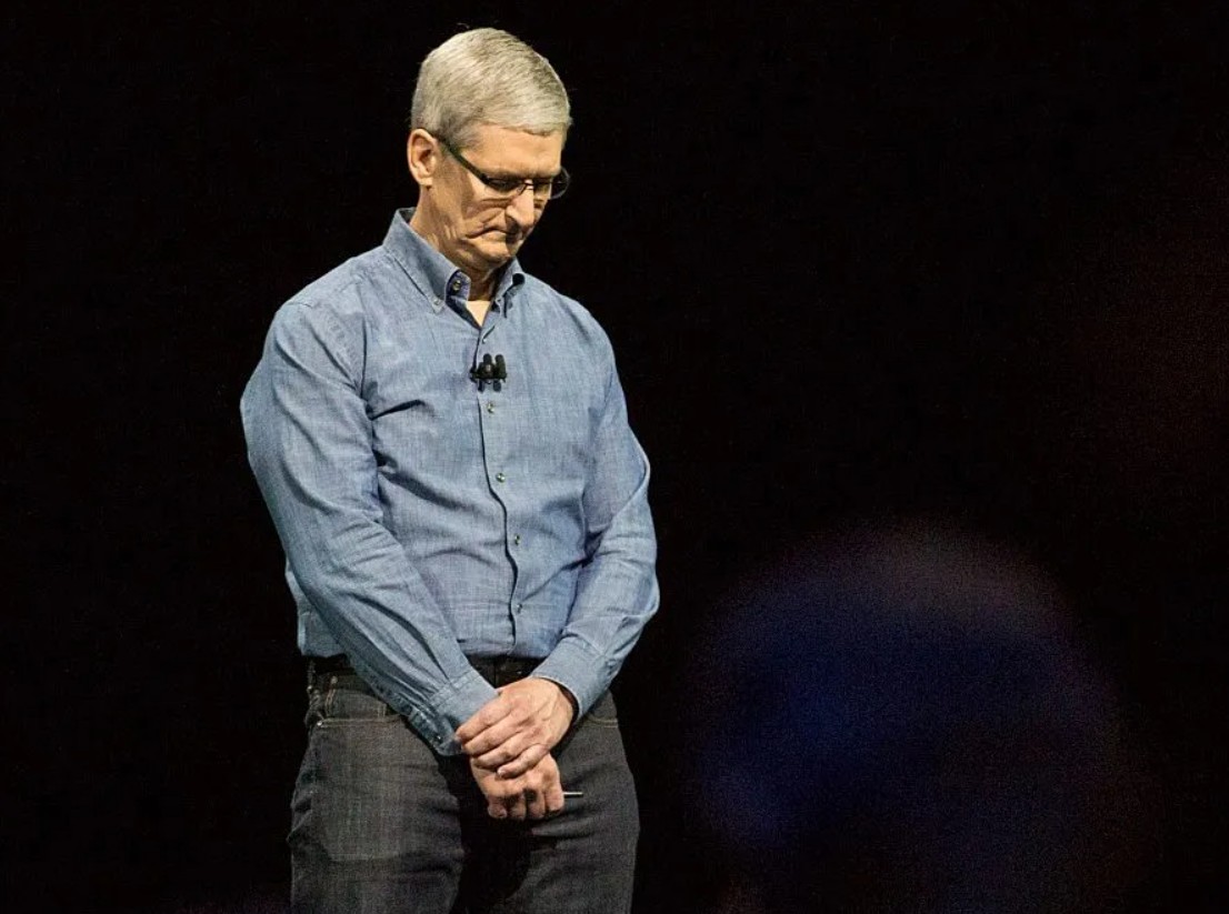 من موقع فون إسلام: يقف رجل يرتدي قميصًا أزرق يشبه جون تيرنوس على خشبة المسرح ورأسه محنيًا رأسه ويديه متشابكتين أمامه على خلفية داكنة.