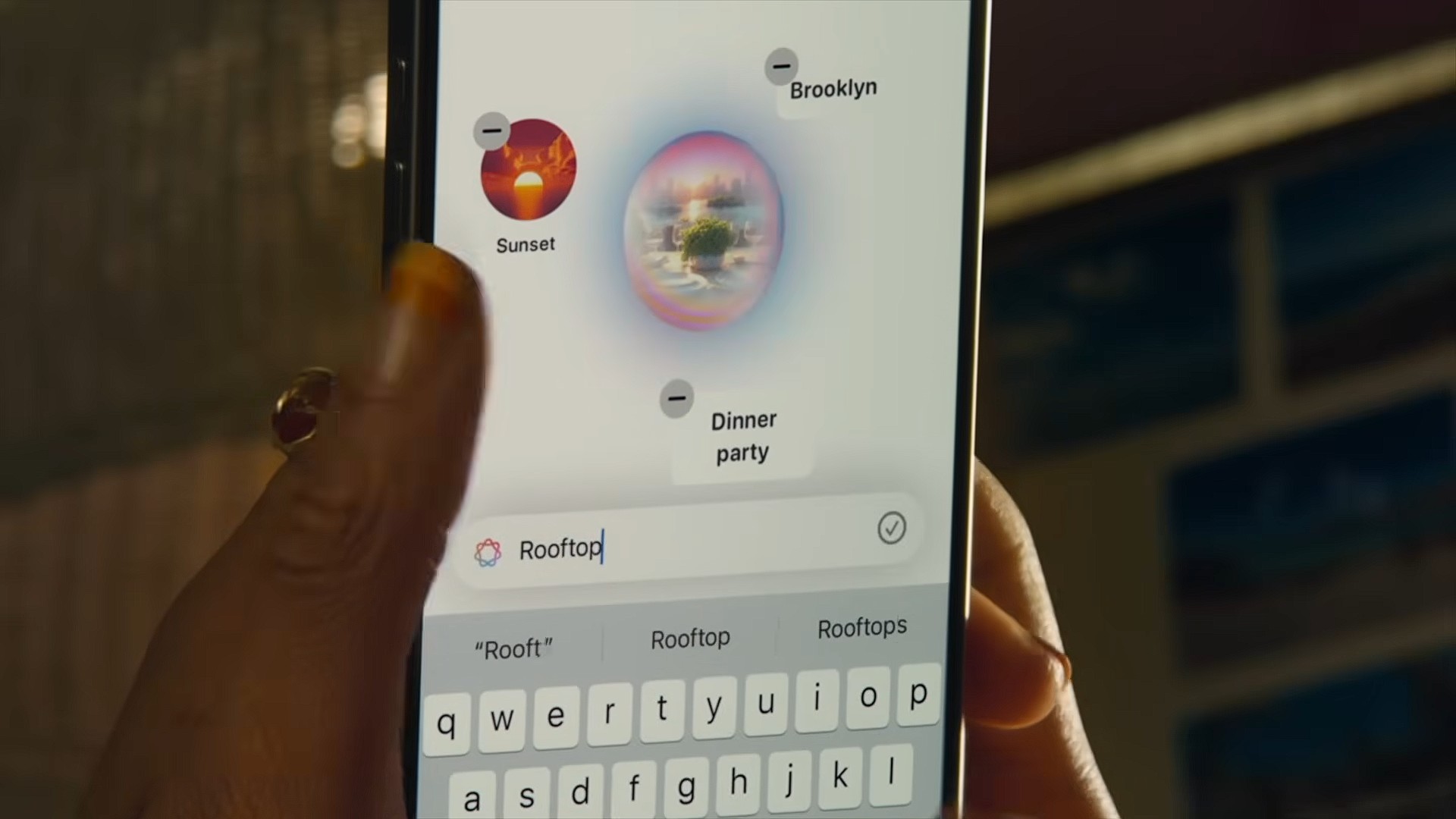 من موقع فون إسلام: شخص يحمل هاتفًا ذكيًا يحمل سيري في نظام iOS 27، ويعرض "غروب الشمس" و"حفلة عشاء" و"بروكلين" على الشاشة أثناء كتابة "السطح" في شريط البحث أعلى لوحة المفاتيح.