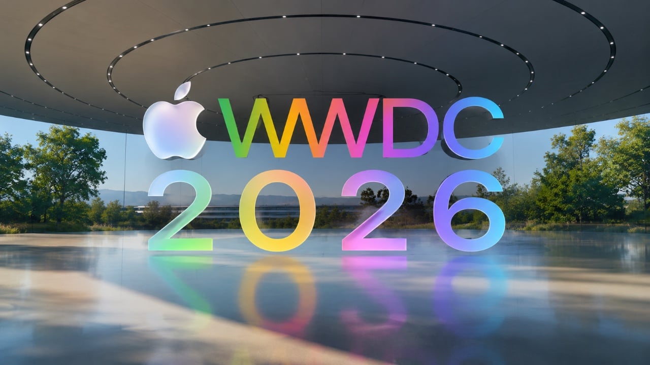 من موقع فون إسلام: نص ثلاثي الأبعاد كبير مكتوب عليه "Apple WWDC 2026" بألوان قوس قزح داخل مبنى زجاجي حديث مع أشجار ظاهرة في الخارج.