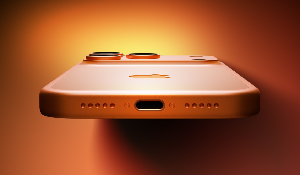 من موقع فون إسلام: لقطة مقربة للحافة السفلية لهاتف ذكي برتقالي اللون مزود بمنفذ USB-C، وفتحات مكبرات صوت تشبه الثقوب الموجودة أسفل هاتف الآيفون، وكاميرات خلفية مزدوجة على خلفية برتقالية.