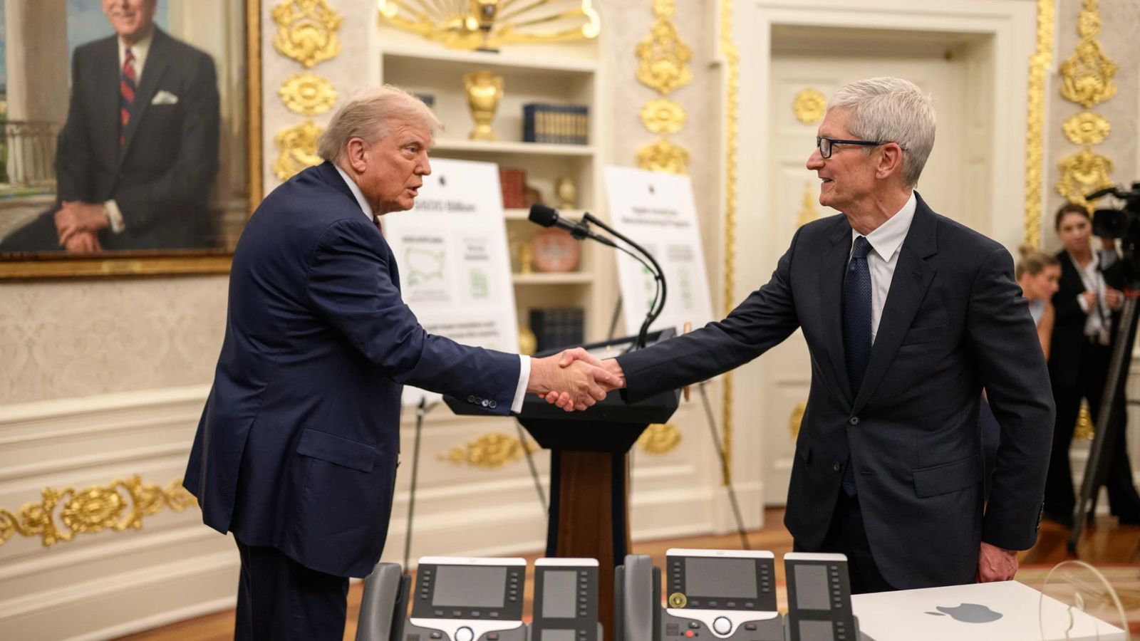 من موقع فون إسلام: رجلان يرتديان بدلات رسمية يتصافحان في غرفة مزينة بزخارف فاخرة مع لمسات ذهبية؛ وتظهر أجهزة إلكترونية على الطاولة في المقدمة، في إشارة إلى المناقشات الحيوية حول أخبار التكنولوجيا الأسبوعية خلال شهر يوليو.