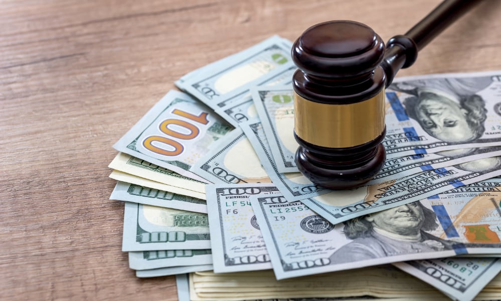 من موقع فون إسلام: مطرقة القاضي موضوعة فوق كومة من الأوراق النقدية فئة المائة دولار المنتشرة على سطح خشبي.