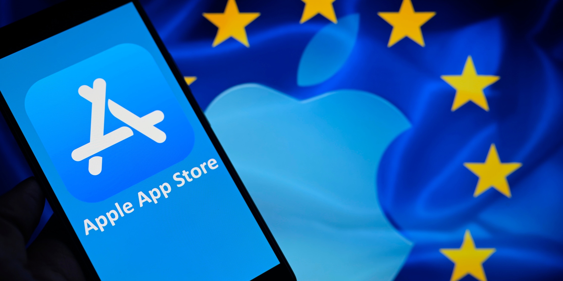 From Phonegram: A smartphone shows the Apple App Store logo and text on it, against a background featuring the Apple logo and the stars of the European Union flag, highlighting the App Store terms in the European Union.
