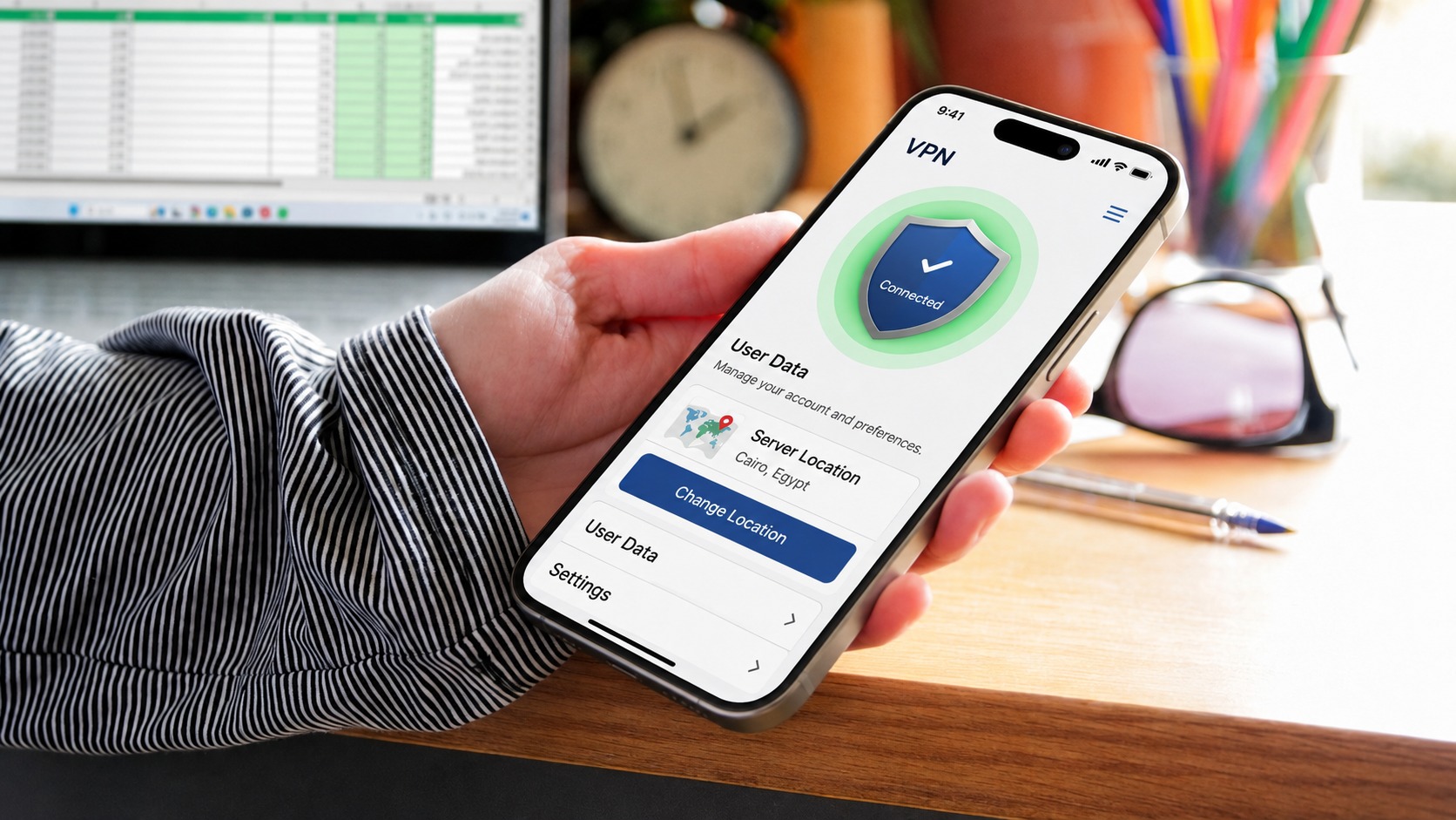 من موقع فون إسلام: شخص يحمل هاتفًا ذكيًّا يعرض تطبيق VPN يظهر عليه «متصل»، مما يضمن الخصوصية والاستخدام الفعال لبطارية الهاتف. ويظهر في الخلفية مكتب عليه جهاز كمبيوتر محمول وساعة ودفتر ملاحظات ونظارات شمسية.