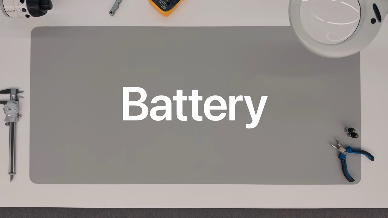 من موقع فون إسلام: طاولة عمل تضم أدوات موضوعة حول سجادة رمادية، تظهر عليها كلمة «Battery» بأحرف بيضاء كبيرة في المنتصف.