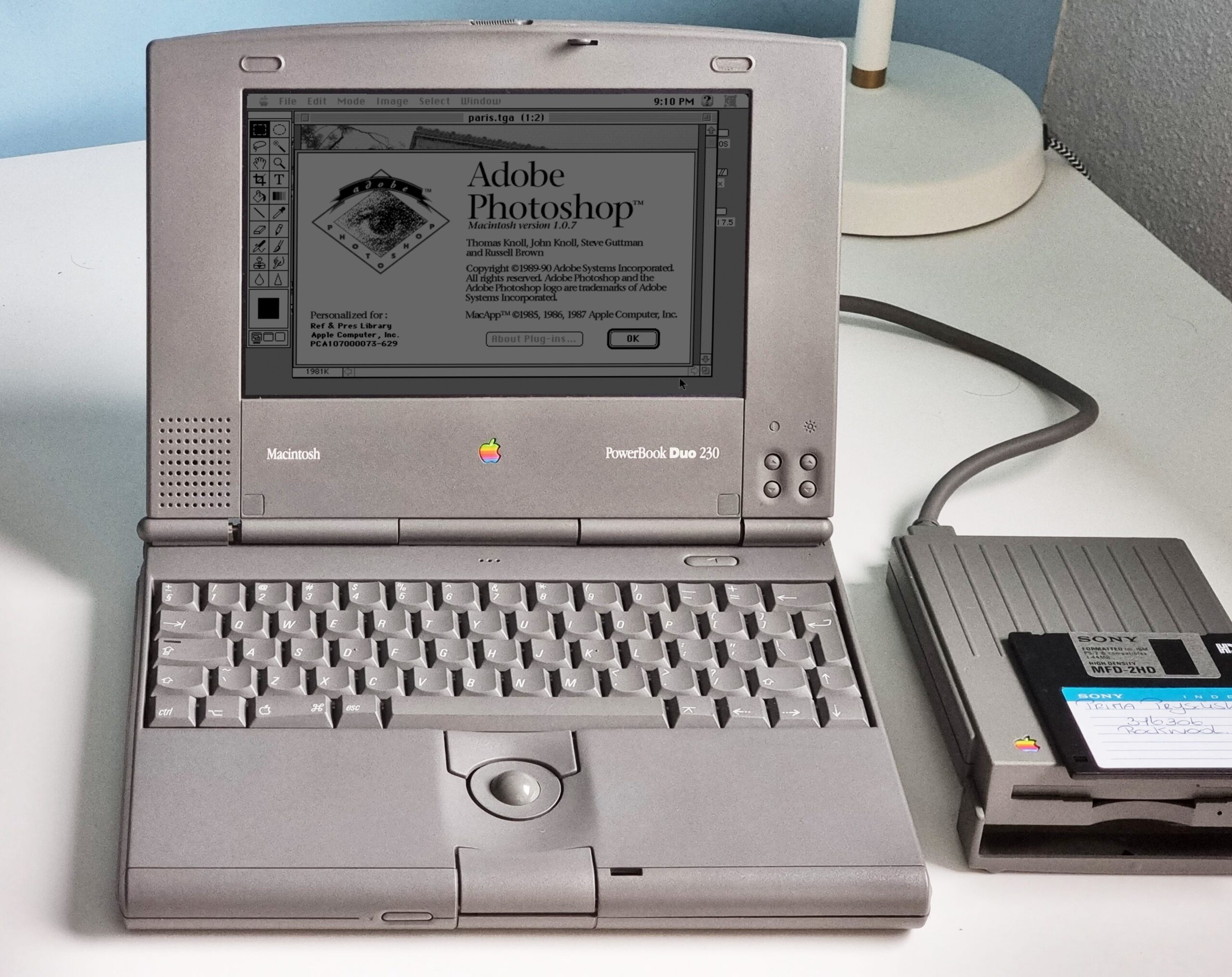 من موقع فون إسلام: يُظهر جهاز كمبيوتر محمول قديم من طراز «Apple PowerBook Duo 230» شاشة بدء تشغيل برنامج «Adobe Photoshop»، مع وجود محرك أقراص مرنة خارجي وقرص مرنة موضوعين بجانبه على المكتب — وهو مشهد يبعث على الحنين إلى الماضي ويُبرز سلسلة التصاميم المبتكرة التي أدت إلى ظهور الأجهزة الحديثة مثل «آي-فون ديو».