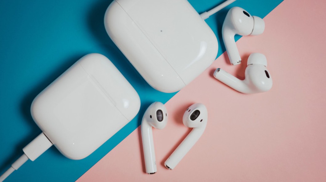 من موقع فون إسلام: زوجان من سماعات «AirPods» اللاسلكية البيضاء مع علبتي الشحن الخاصتين بهما، على خلفية مقسمة إلى اللونين الأزرق والوردي.