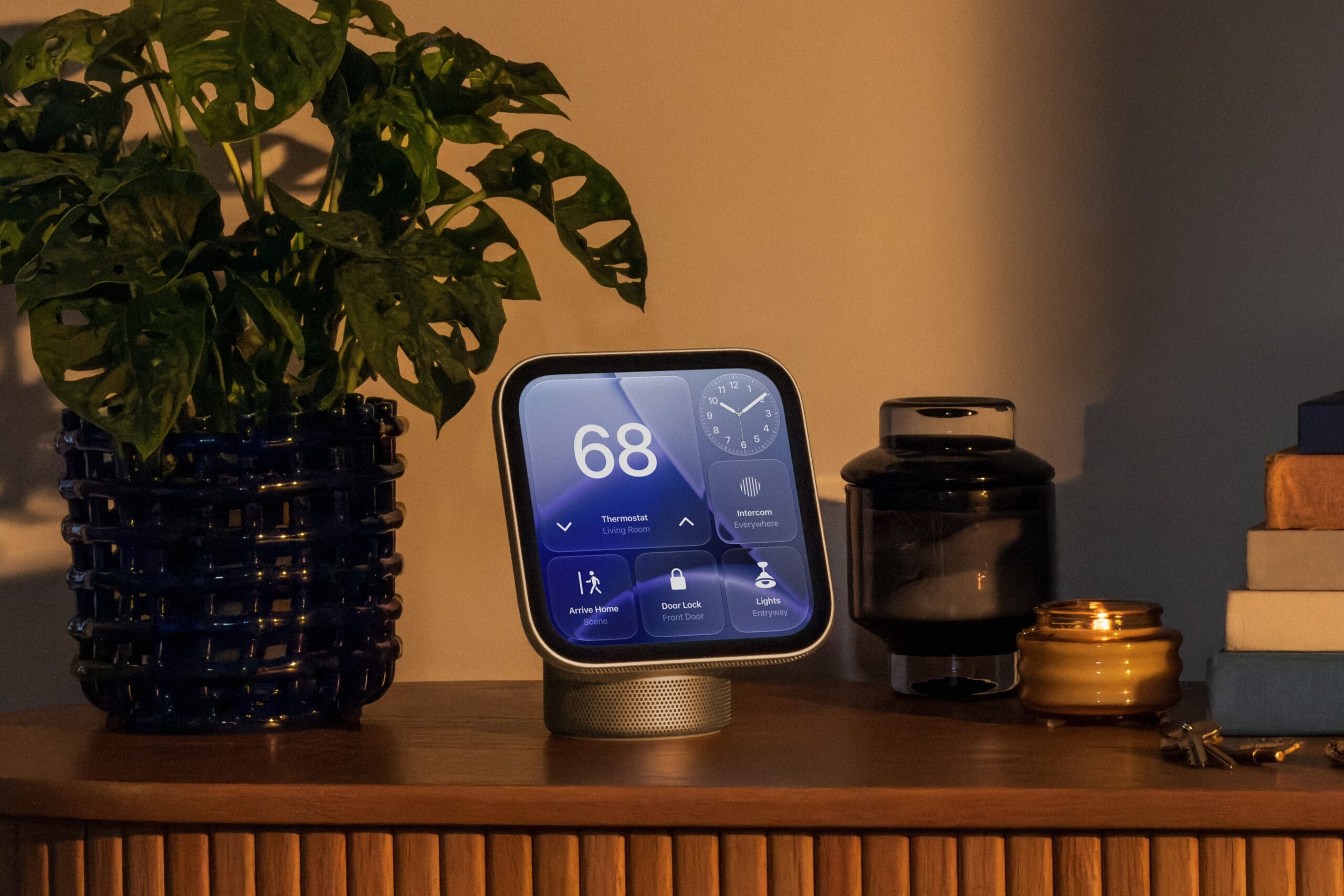 من موقع فون إسلام: تُظهر «Apple Home View» جهاز ترموستات مضبوط على 68 درجة، مزودًا بأزرار للتحكم في جهاز الاتصال الداخلي والإضاءة وقفل الباب، وهو موضوع على سطح خشبي بجوار نبتة وشموع.