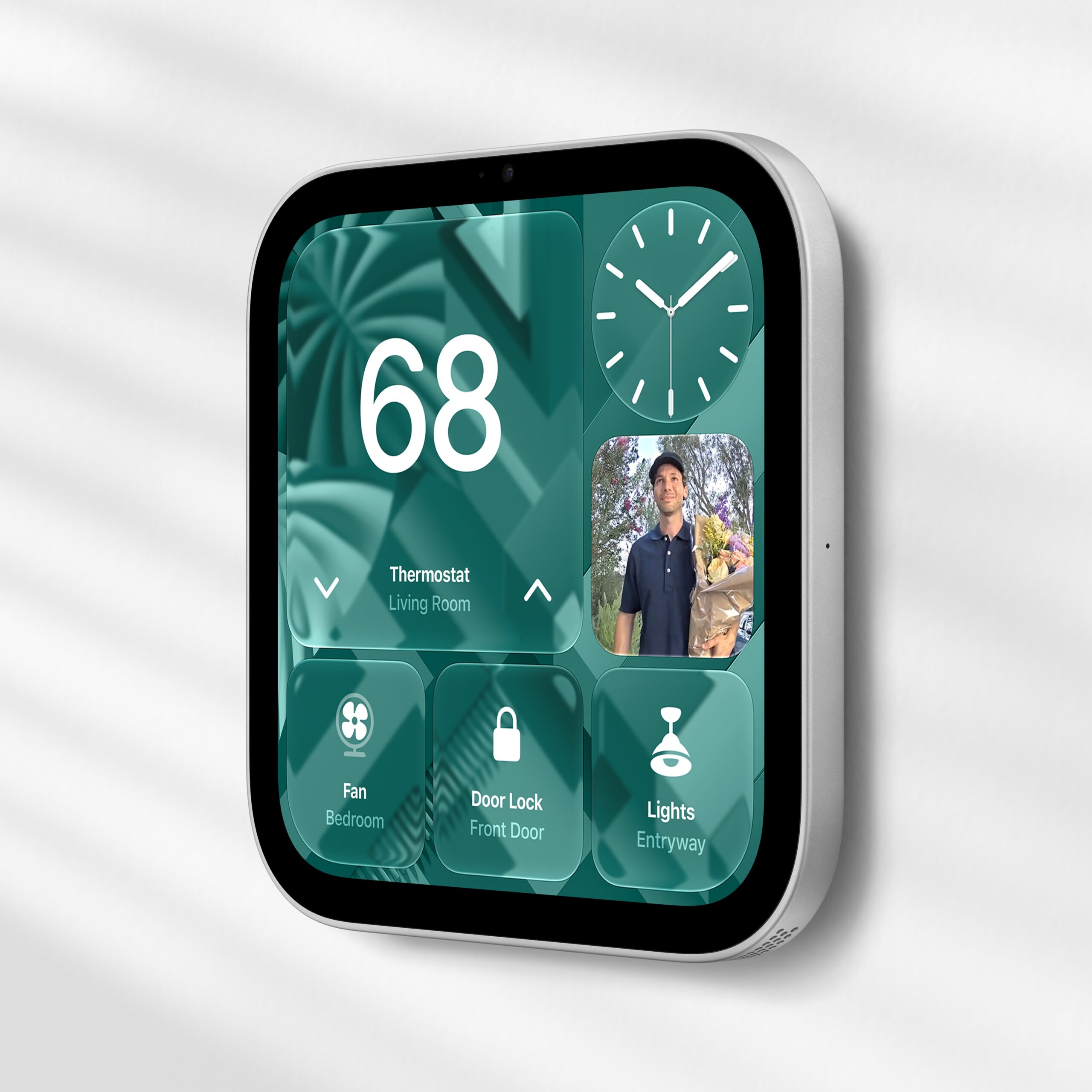 من موقع فون إسلام: شاشة «Apple Home View» مثبتة على الحائط تعرض إعدادات منظم الحرارة، وساعة، وصورة مباشرة من جرس الباب المزود بكاميرا، وأزرار التحكم في مروحة غرفة النوم، وقفل الباب الأمامي، وأضواء المدخل.