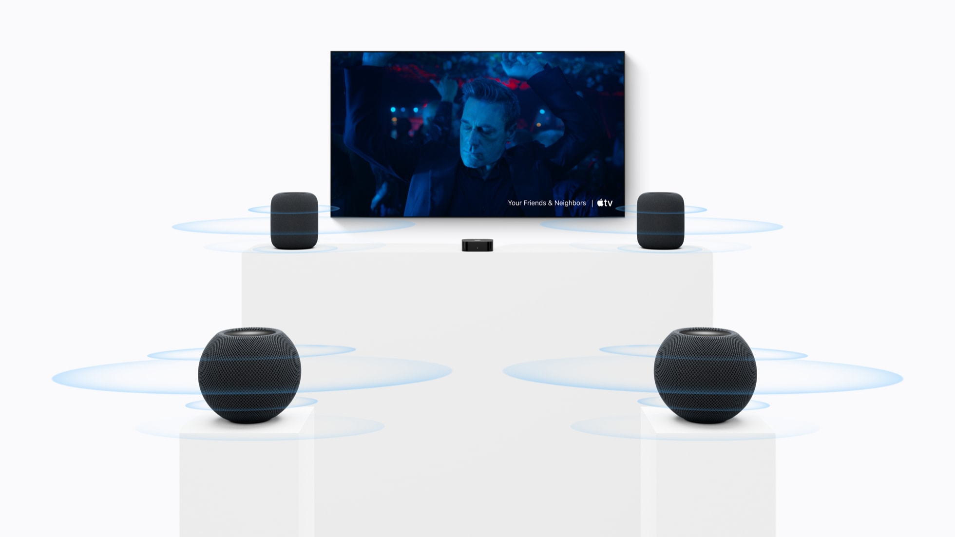 من موقع فون إسلام: أربعة مكبرات صوت من طراز HomePod mini 2 موزعة حول شاشة تلفزيون تعرض مشهدًا من فيلم «Your Friends & Neighbors» على Apple TV، مع موجات دائرية زرقاء تشير إلى صوت محيطي غامر.