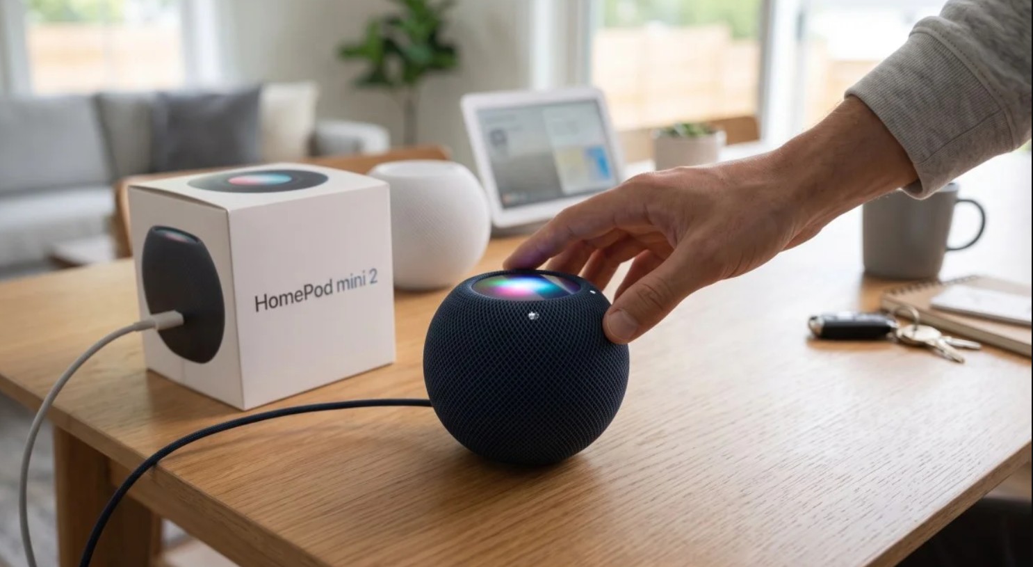 من موقع فون إسلام: تتجه يد نحو مكبر صوت ذكي من طراز HomePod mini 2 باللون الأزرق الداكن، موضوعًا على طاولة خشبية بجوار عبوته.